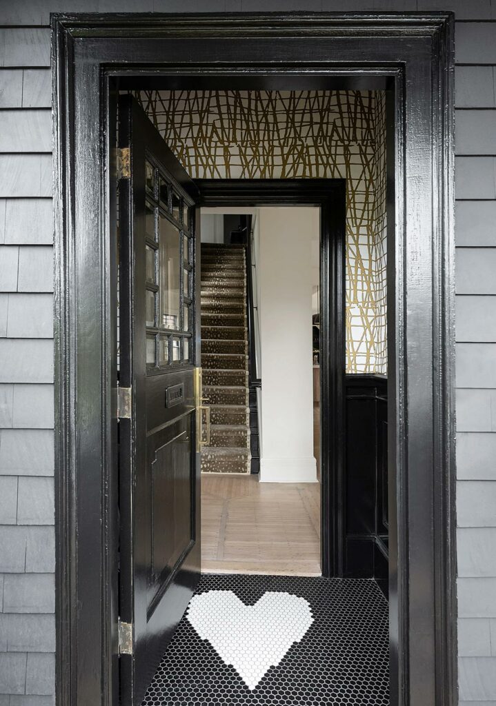 An entrance framed in black painted wood trim with black hexagonal tile on the floor with an inlaid heart shape in white tile