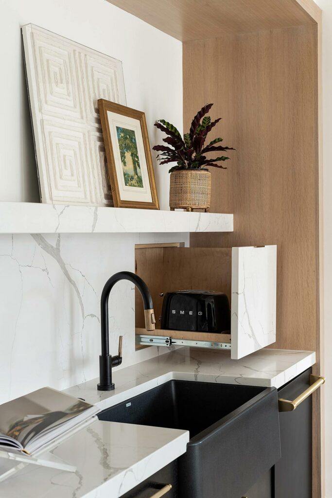 View of the kitchen with black undermount sink, bronze fixtures, and a toaster on a sliding pull out cabinet shelf.